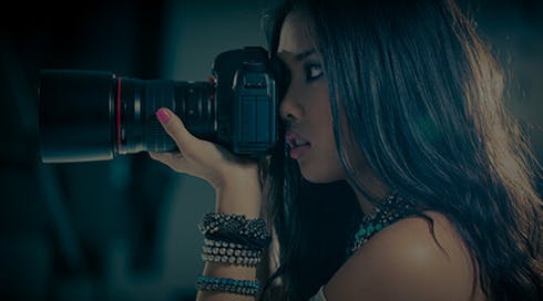 tan girl with dark hair holding a large camera and taking a picture
